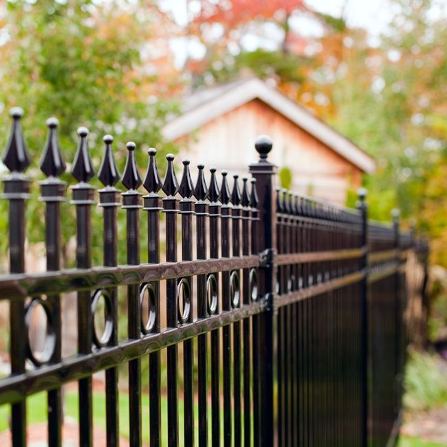 Black wrought-iron fence in front of a blurred house and autumn trees