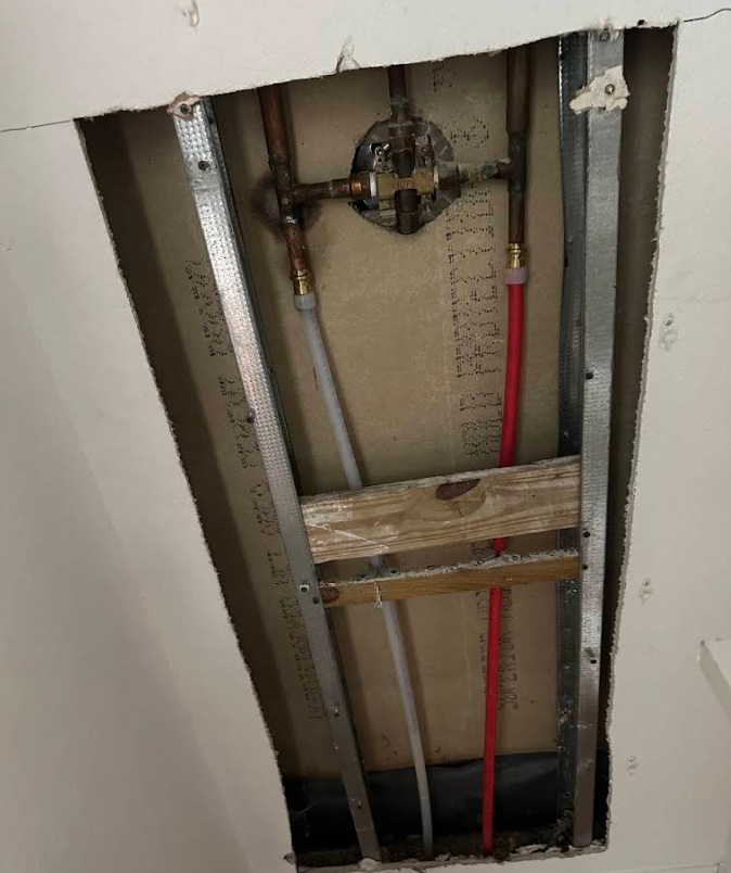 Open wall cavity with exposed plumbing pipes, red conduit, and wooden bracing.