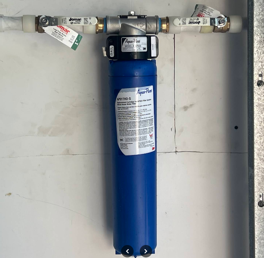 Blue water filter mounted on a wall with metal pipes and shutoff valves.