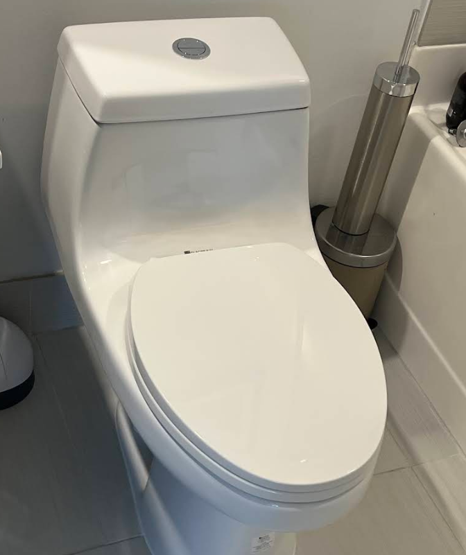 White toilet in a bathroom beside a silver toilet brush holder.