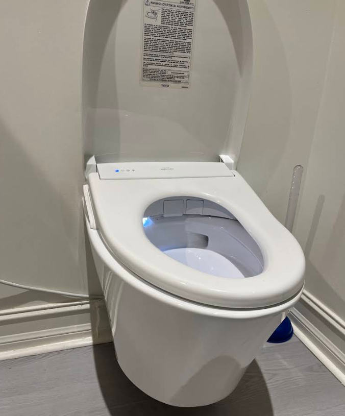 White toilet in an accessible restroom stall with raised seat and blue grab handle.