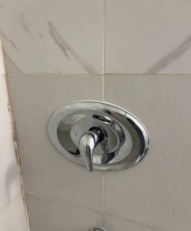 Chrome shower control knob on white tiled bathroom wall