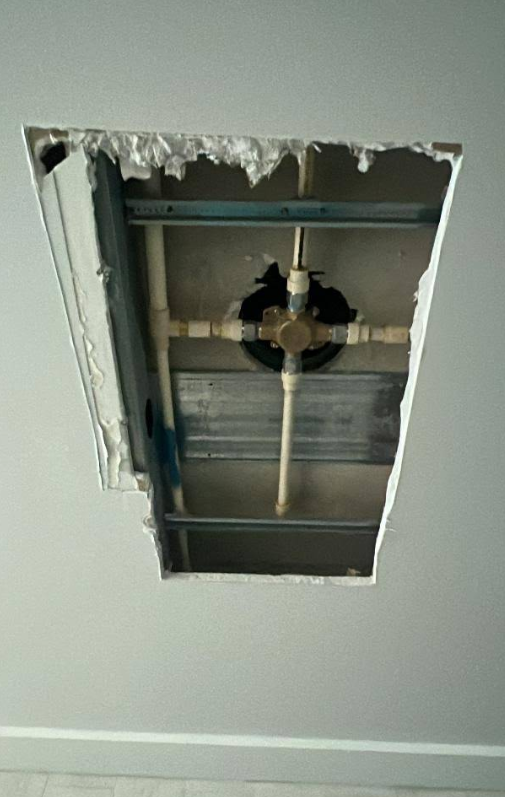 Open ceiling drywall cutout exposing pipes and framing in a room