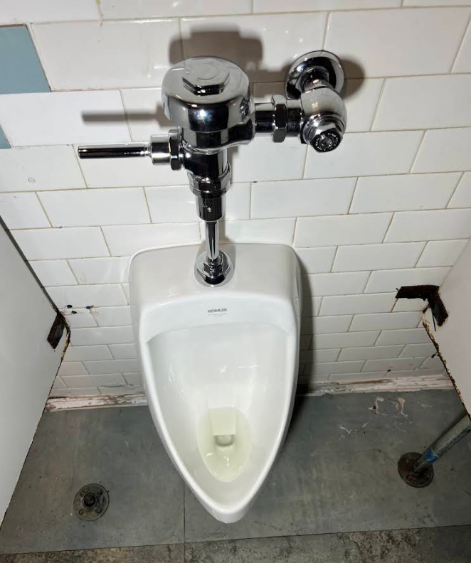 Public restroom urinal with chrome flush valve and white tile wall