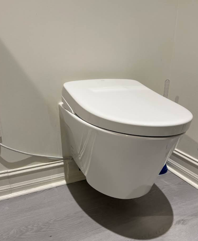 White wall-mounted toilet in a minimalist bathroom corner with gray floor and baseboard trim