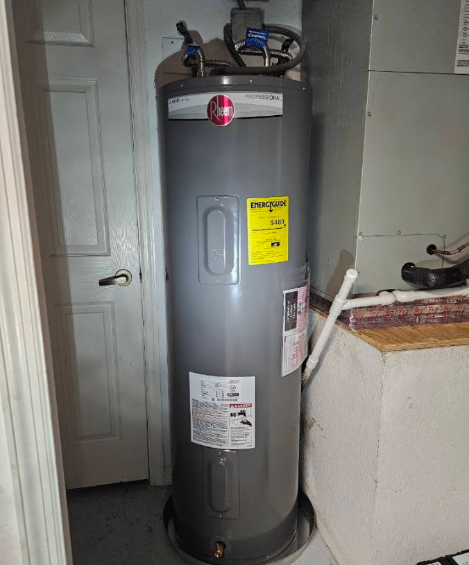 Gray water heater in a utility room beside a door and countertop, with warning labels and pipes on top.