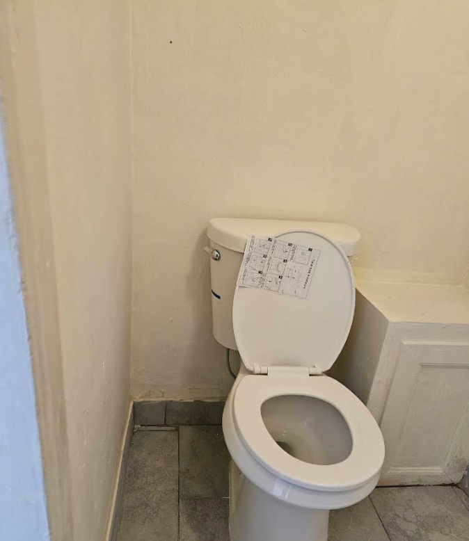 Small bathroom with a white toilet next to a beige wall and tiled floor.