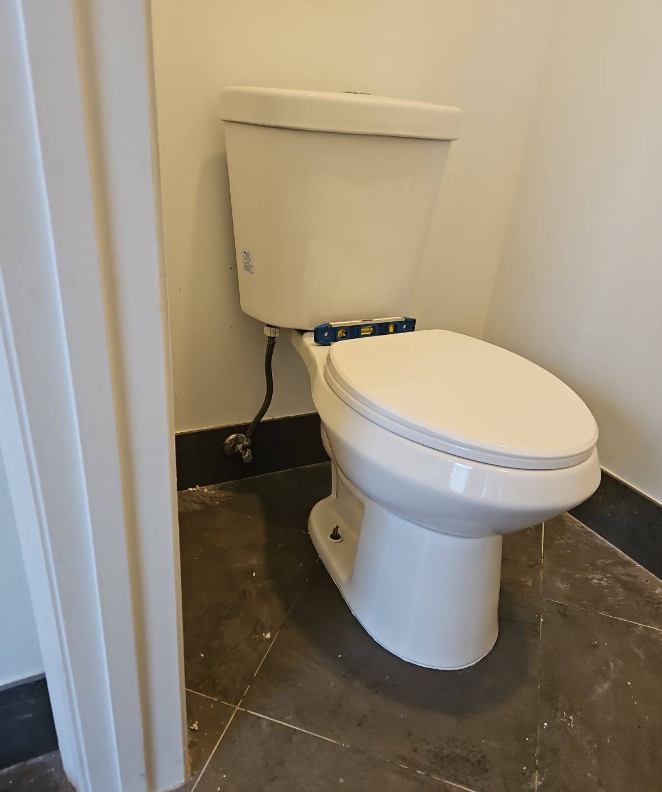White toilet in a small bathroom with black marble floor tiles and beige walls.