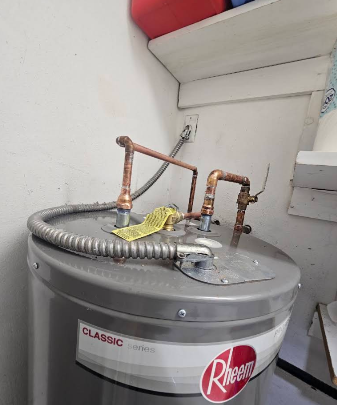 Rheem water heater with copper piping and gray flexible vent hose in a utility closet