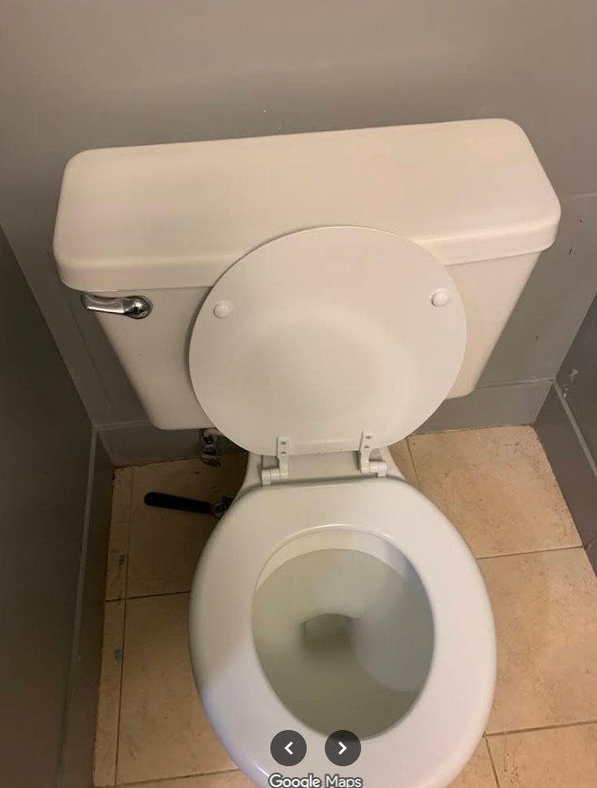 Open toilet with white tank and lid in a beige-tiled bathroom.