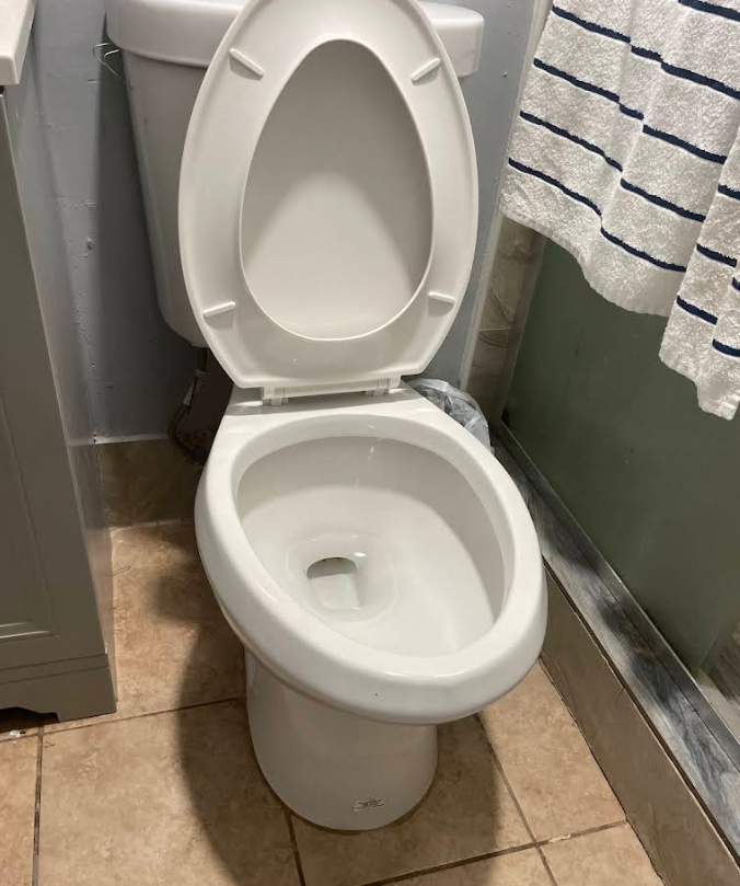 Open toilet in a small bathroom with tan tile floor and striped towels nearby
