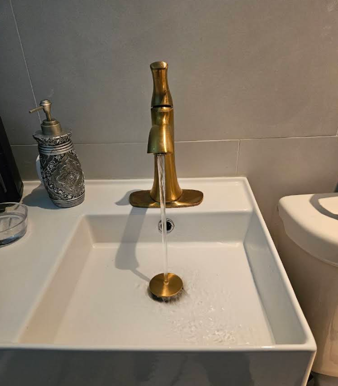 Brass bathroom faucet filling a white square sink with a matching brass drain cover