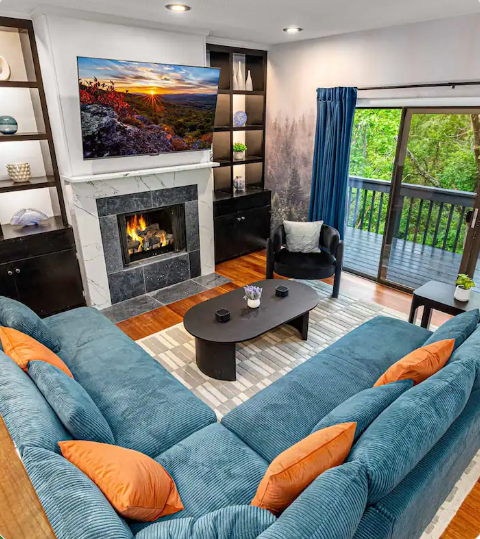 Cozy living room with blue sectional, fireplace, coffee table, and sliding doors to a balcony and greenery