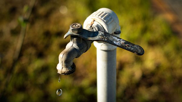 Leaky outdoor water faucet with a dripping drop against a blurred background
