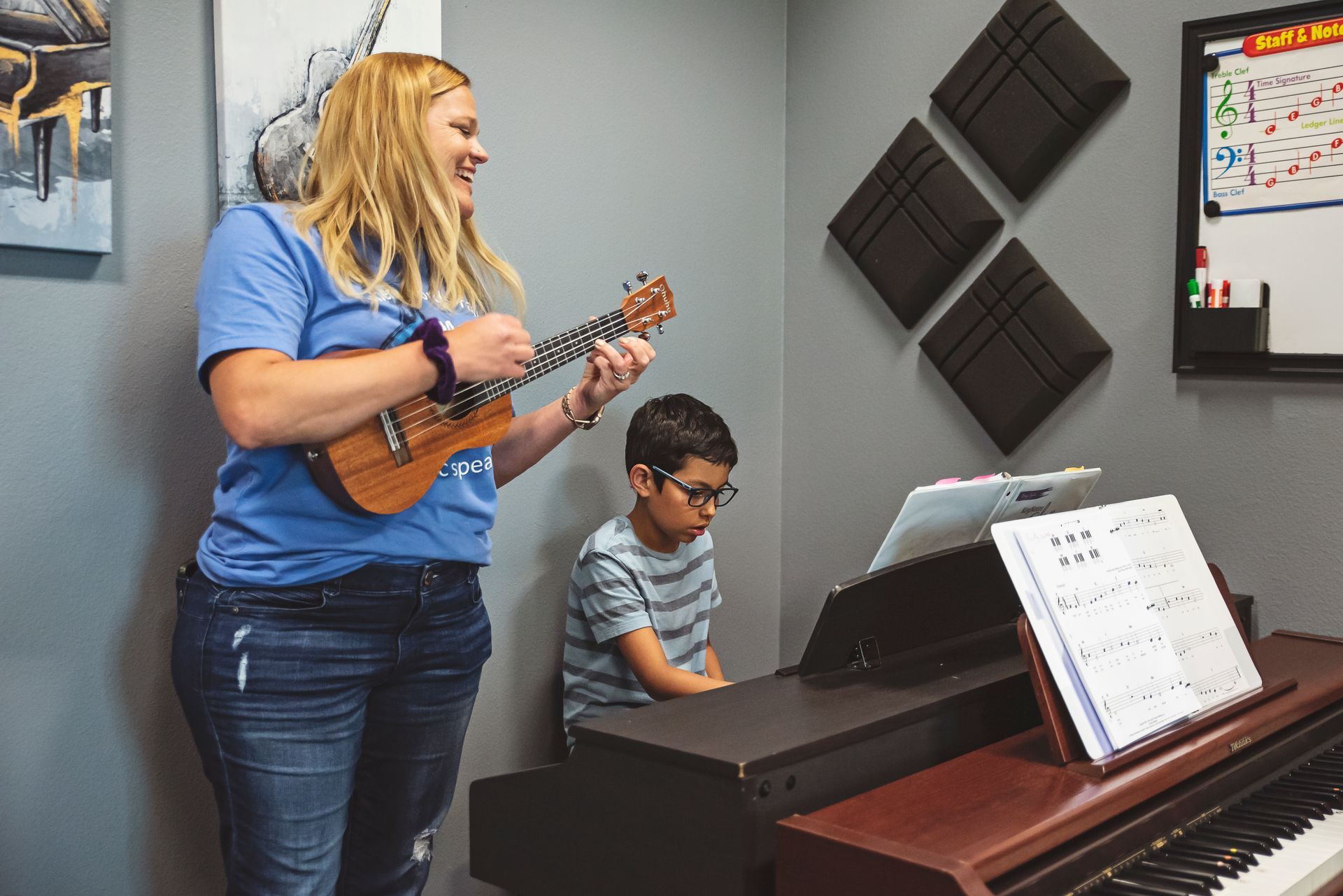 A woman is playing a ukulele and a boy is playing a piano.