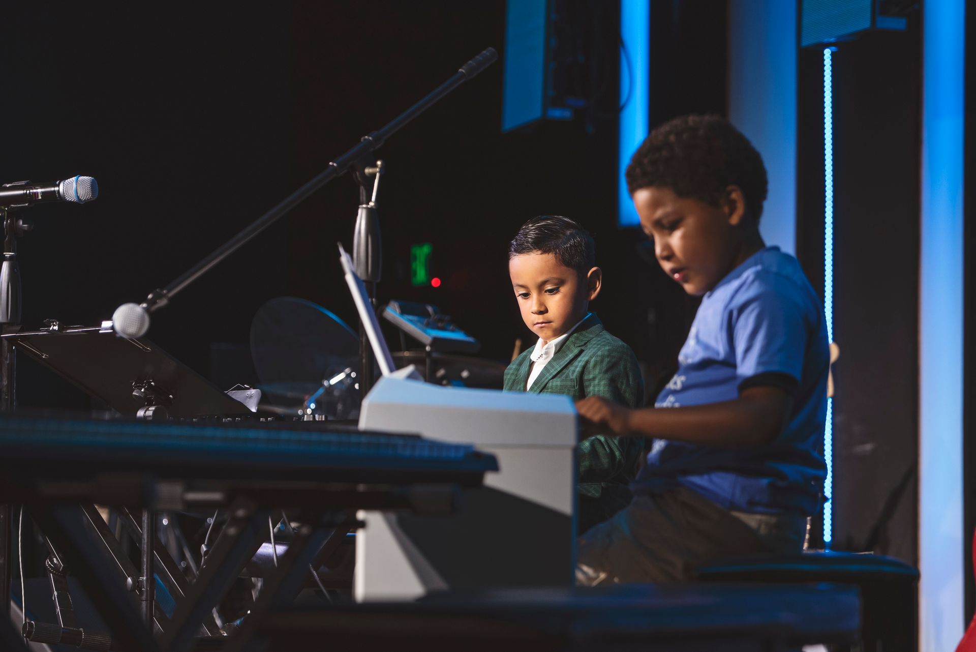 Two young boys are playing keyboards on a stage.