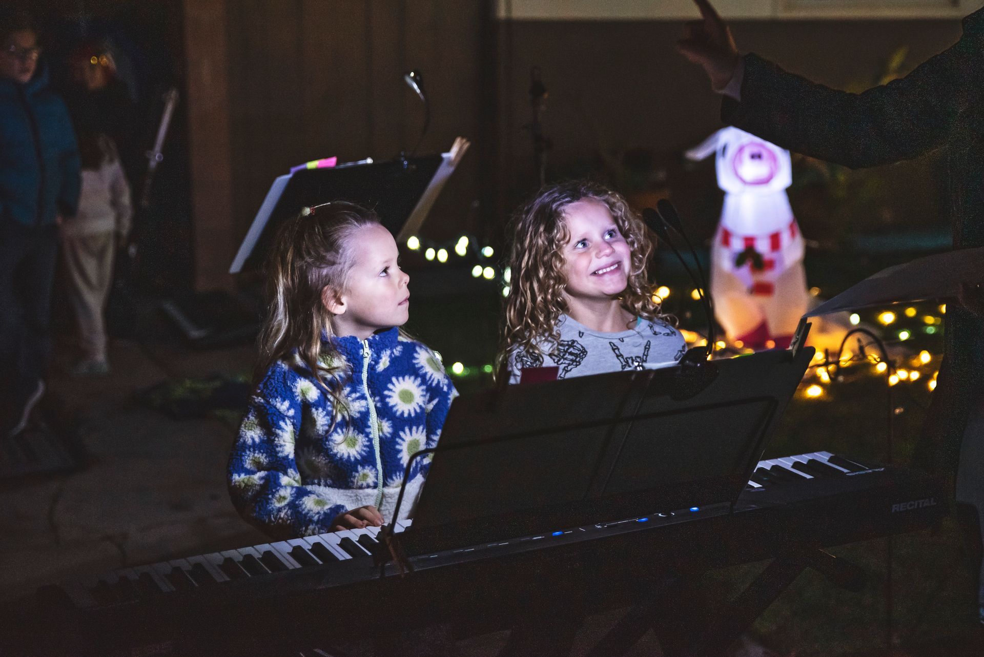 Two little girls are sitting at a piano in a dark room.
