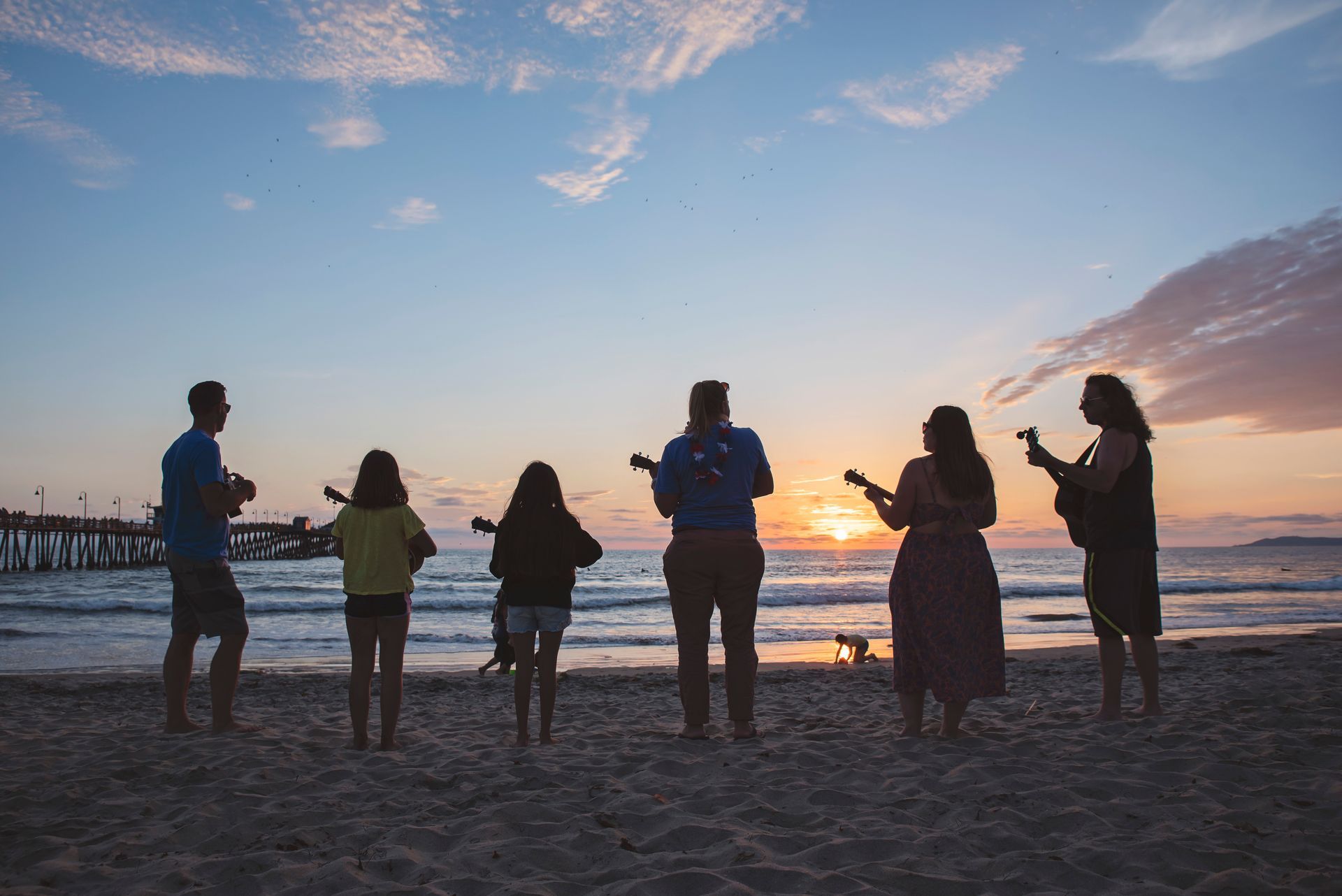 A group of people are playing ukuleles on the beach at sunset.