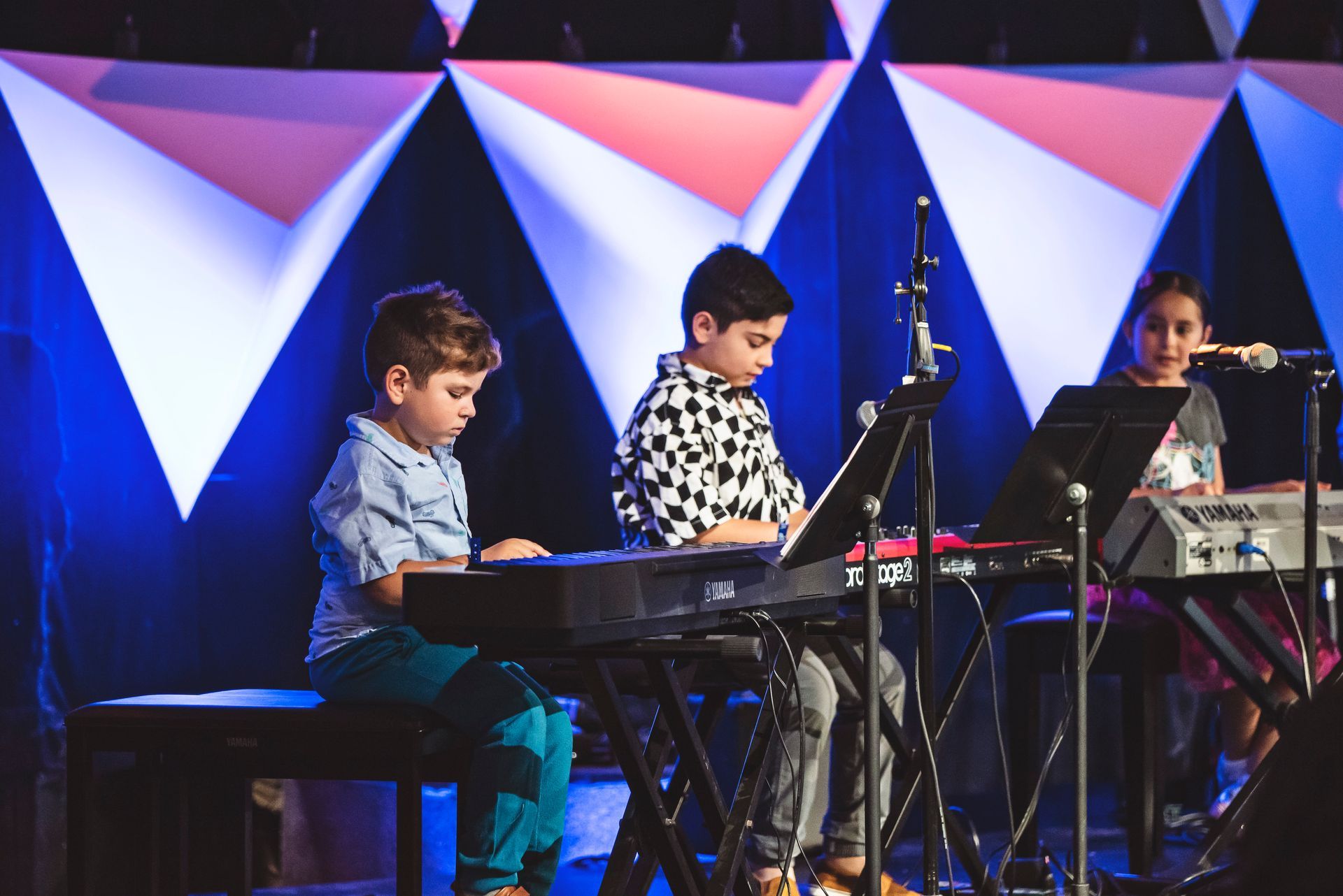 Three young boys are playing keyboards on a stage.