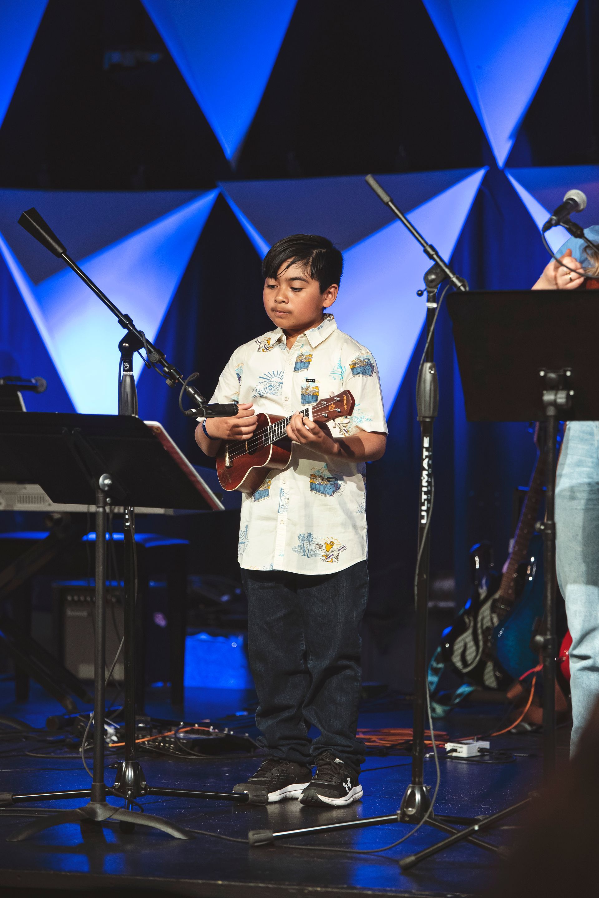 A young boy is playing an ukulele on a stage.