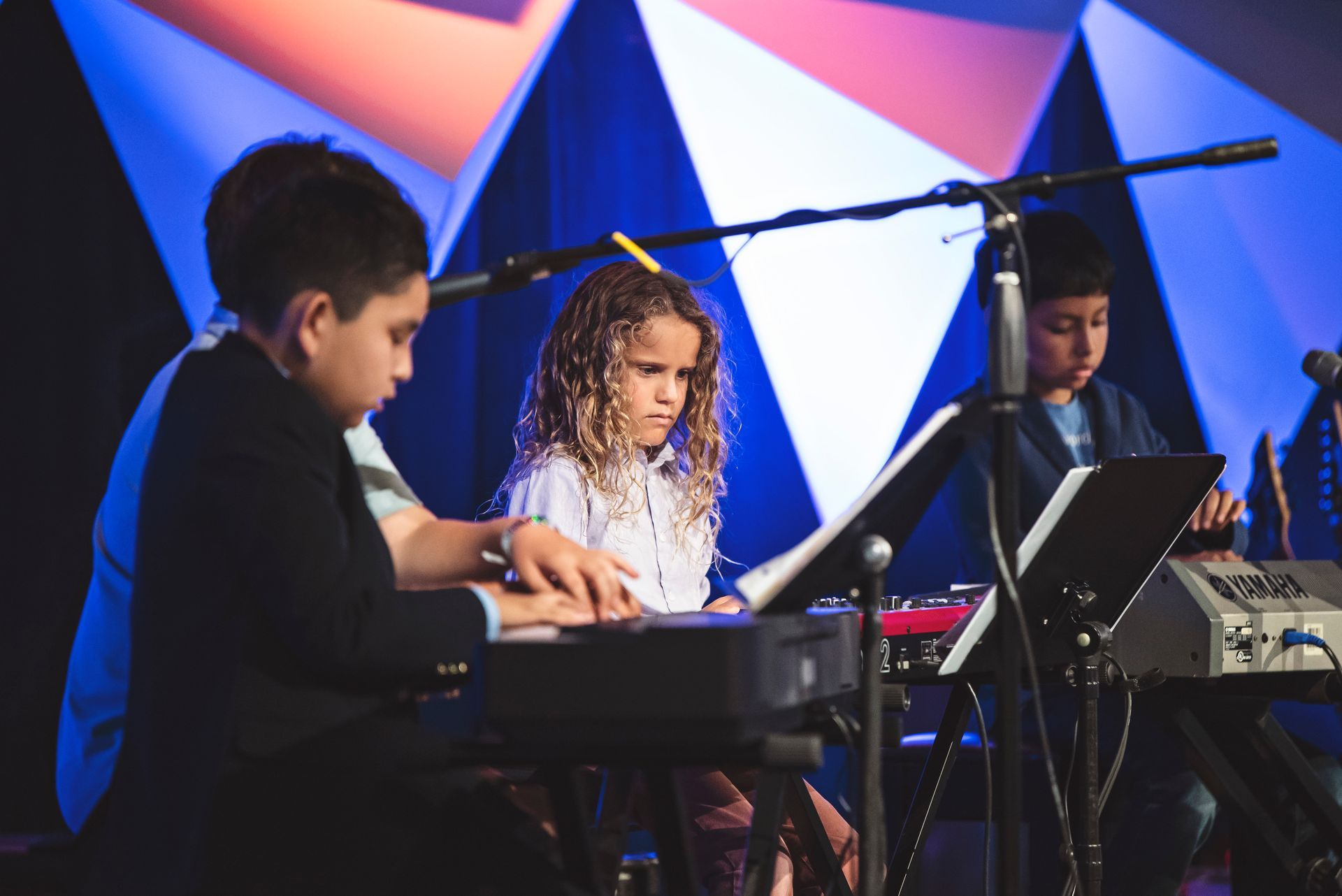 A group of children are playing keyboards on a stage.