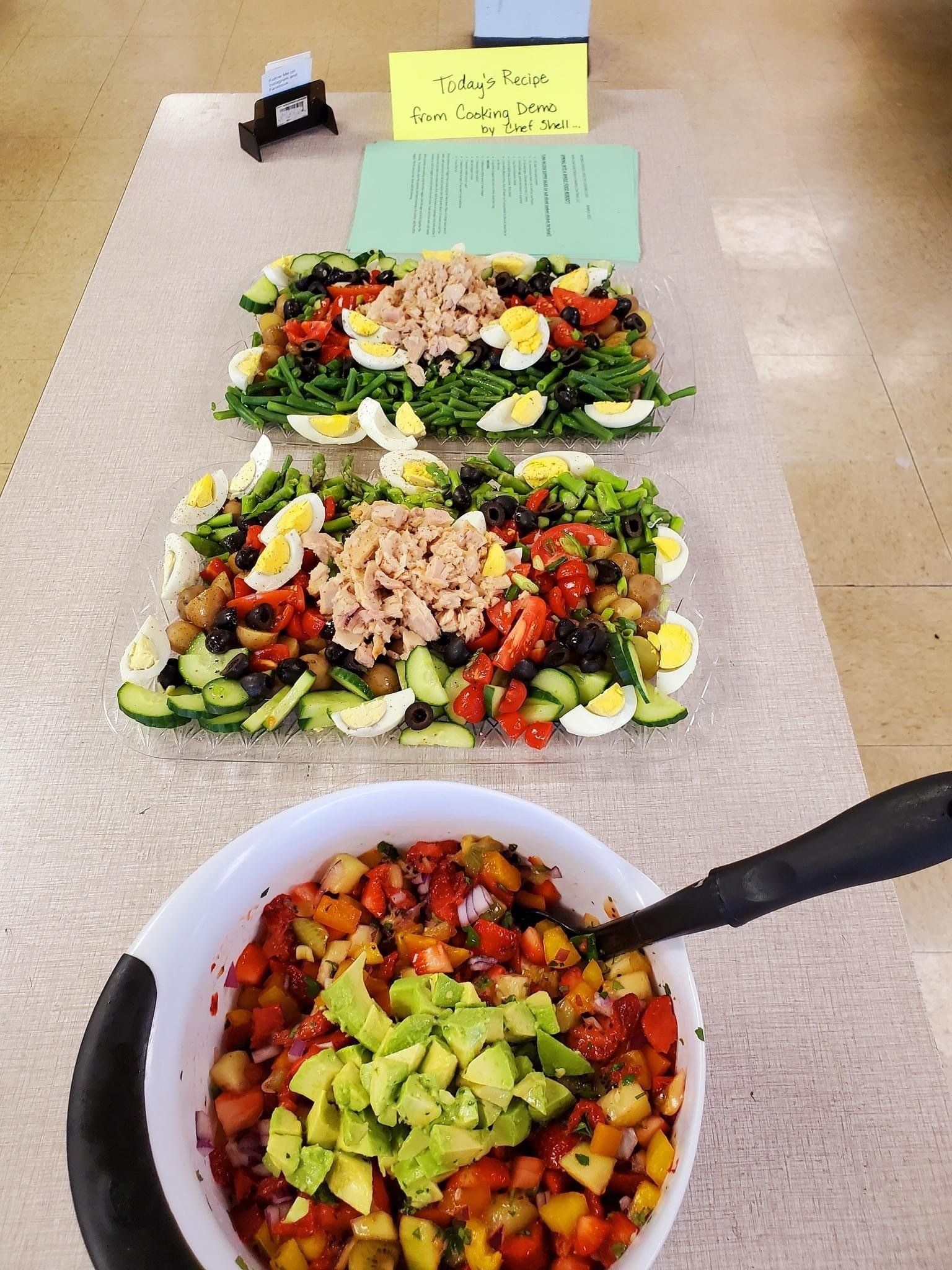 A bowl of guacamole sits on a table next to a tray of salads