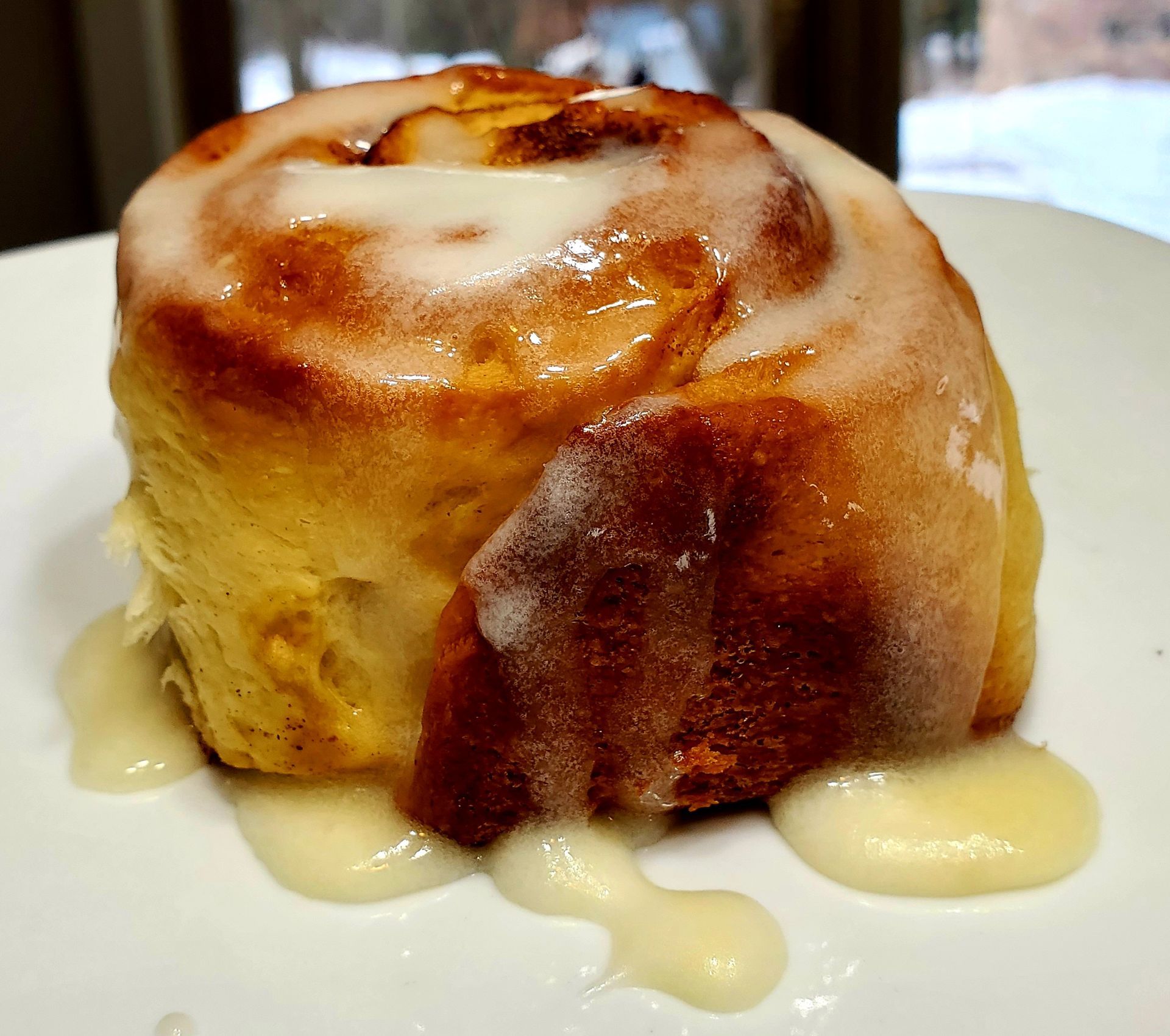 A cinnamon roll with icing on it is on a white plate.