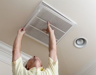 Person adjusting a ceiling air vent in a room, reaching up with both hands.