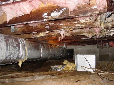 Crawlspace with exposed ductwork, damaged insulation, and water damage on floor joists