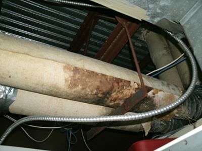 Corroded pipe with rust, wrapped in insulation and metal conduit inside a cramped utility space