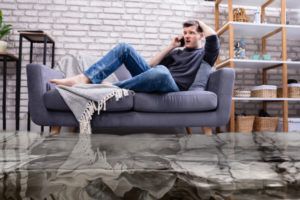 Person reclining on a gray sofa in a living room with a brick wall and shelves.