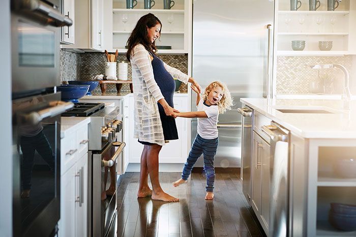 Woman and small child holding hands in a bright kitchen near a stainless steel refrigerator