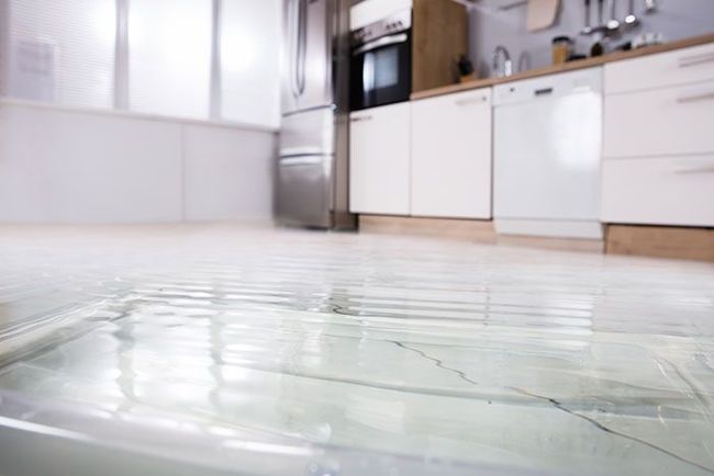Kitchen floor flooded with water near white cabinets and a stainless-steel refrigerator