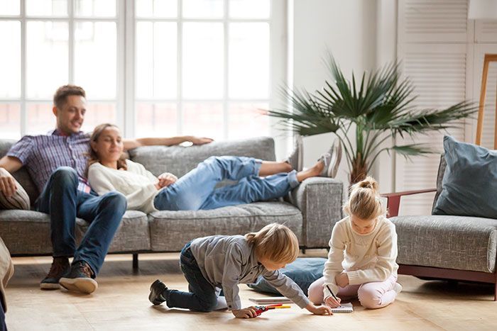 Family relaxing on a couch while two children play on the floor in a bright living room.