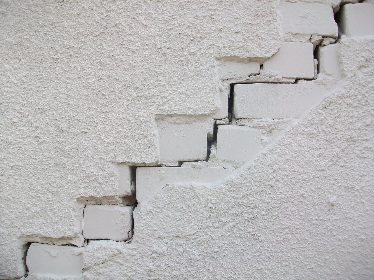 Cracked plaster wall with a stepped diagonal gap exposing bricks underneath