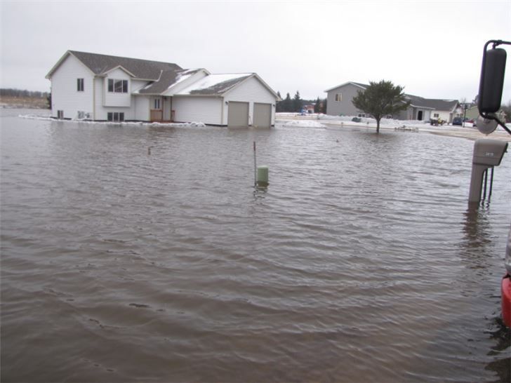 Homes surrounded by floodwater on a cloudy day, with a road sign partly submerged