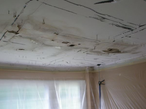 Water-damaged ceiling with peeling paint above a window in a room under repair