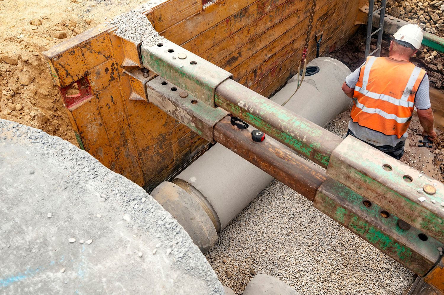 A construction worker is working on a pipe in a trench.