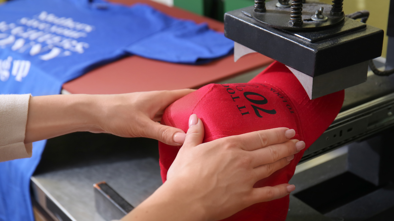Person using a heat press to apply a design to a red baseball cap.