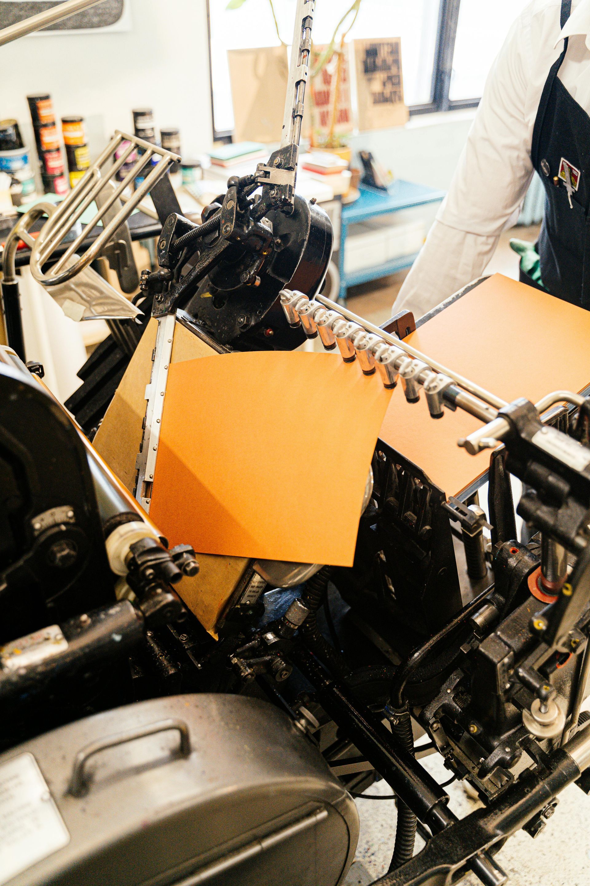 Person operating an orange sheet printing press in a workshop.