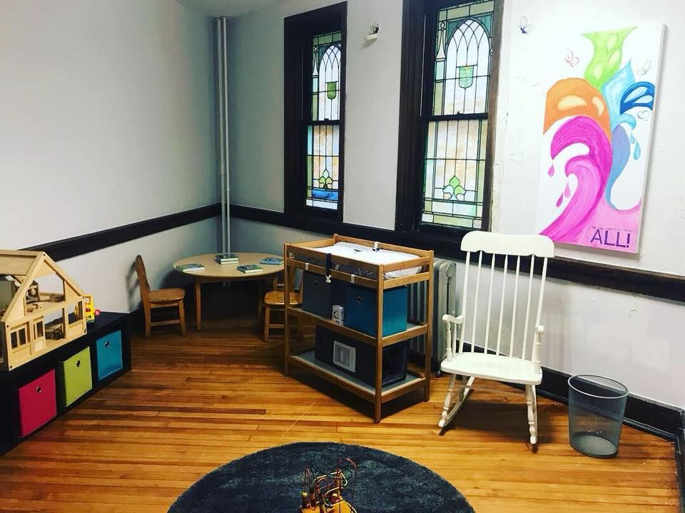 Short North Church. Empty classroom corner with colorful furniture, two stained-glass windows, and a child’s artwork on the wall