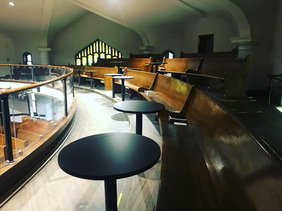 Short North Church. Empty indoor seating area with round black tables, wooden benches, and arched windows in dim light