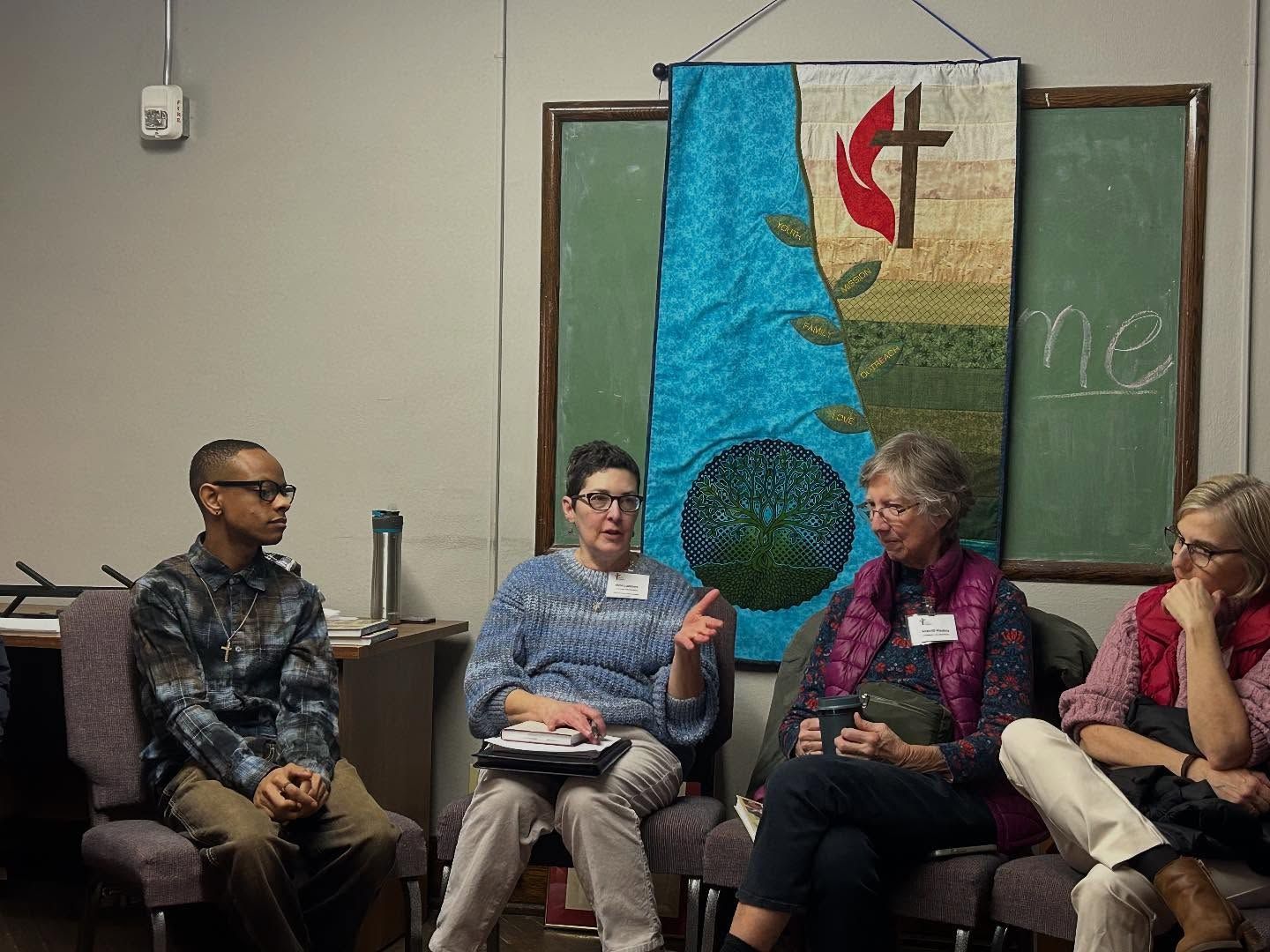 Short North Church. Four people seated in discussion before a green chalkboard and colorful hanging banner