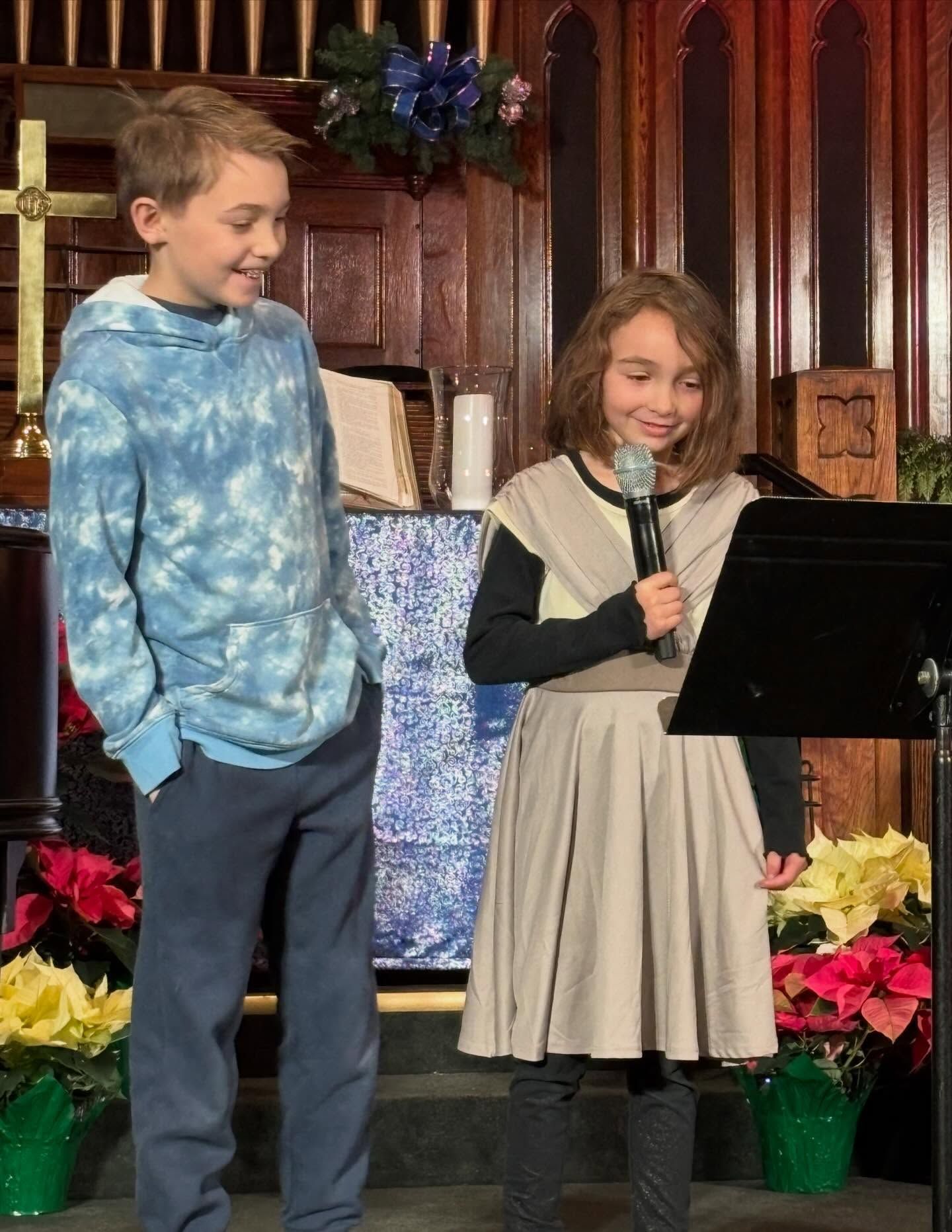 Short North Church. Two children stand at a podium in a church, one holding a microphone and reading from a script.
