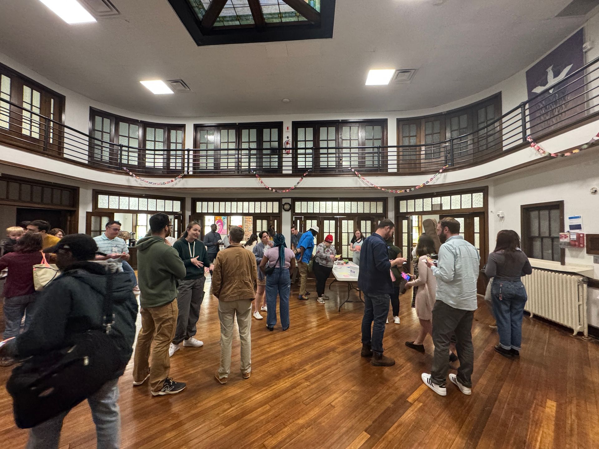 Short North Church. People gathered in a bright hall with polished wood floors and white walls, talking in small groups.