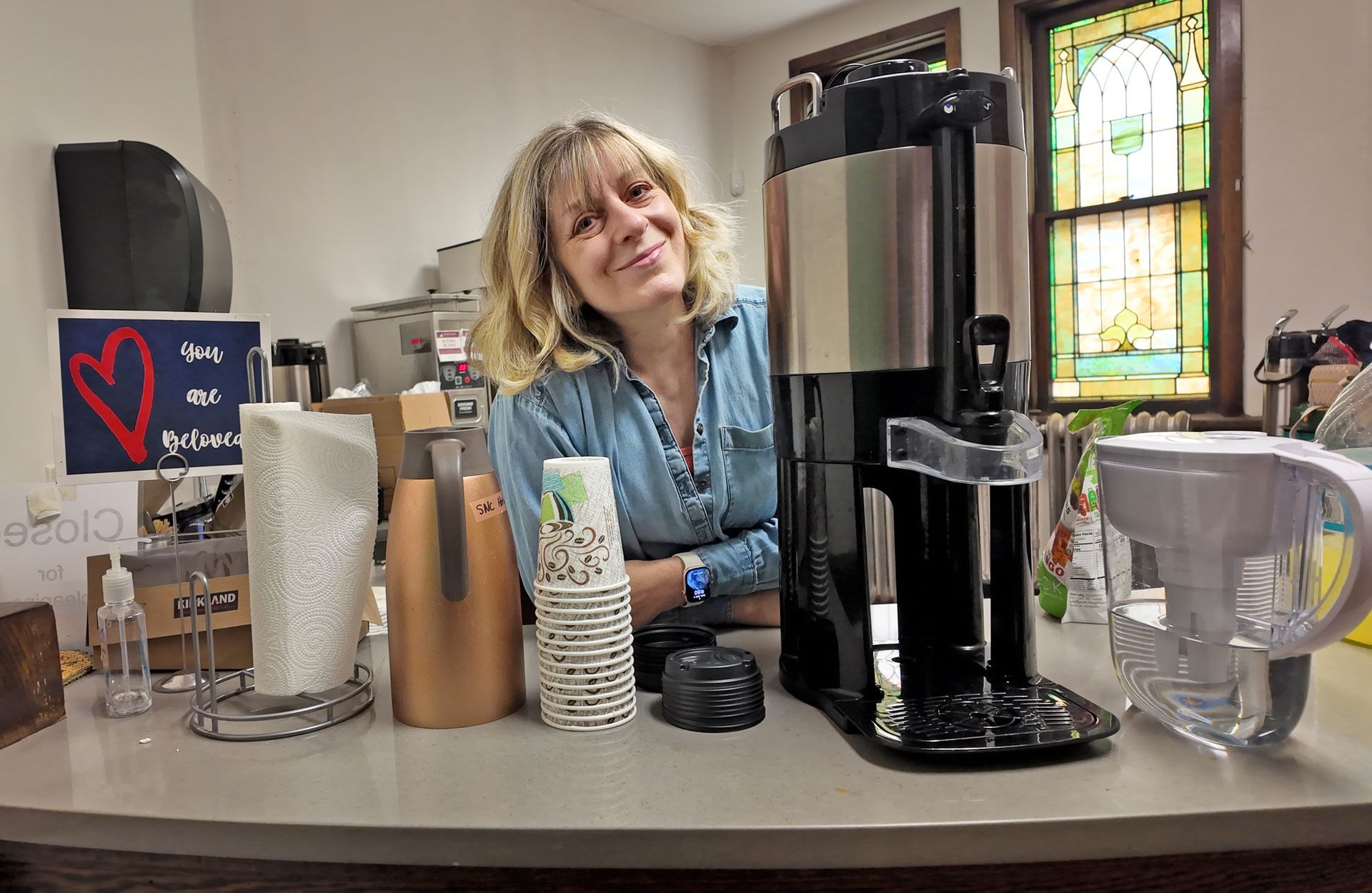 Short North Church. Woman behind coffee counter with espresso machine, cups, and a stained-glass window in the background