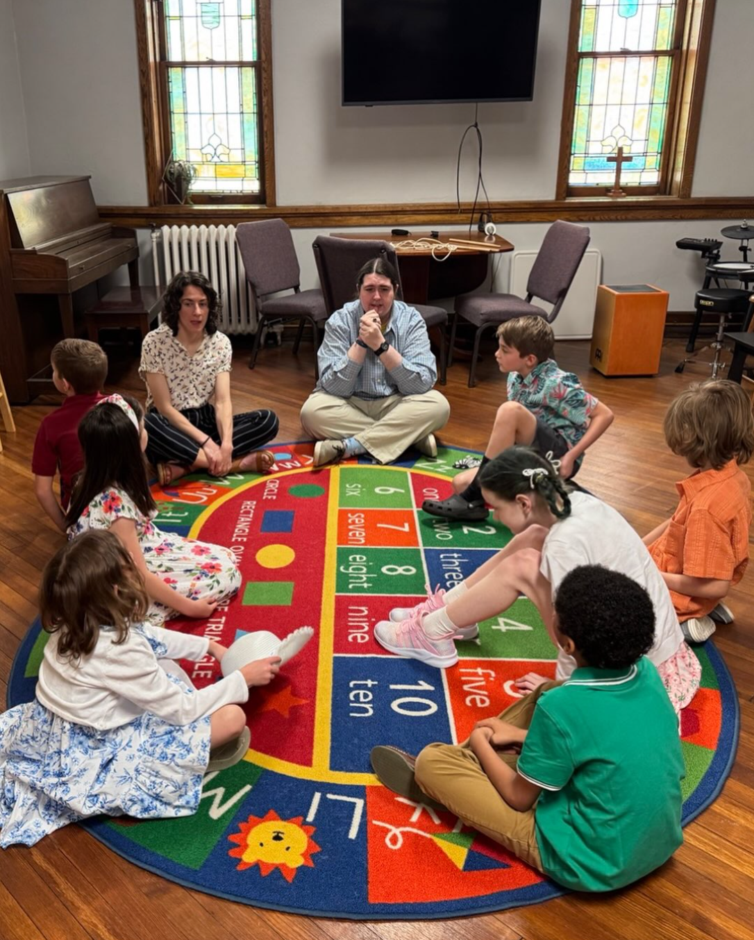 Short North Church. People sitting in a circle on a colorful alphabet rug during a group activity in a room.