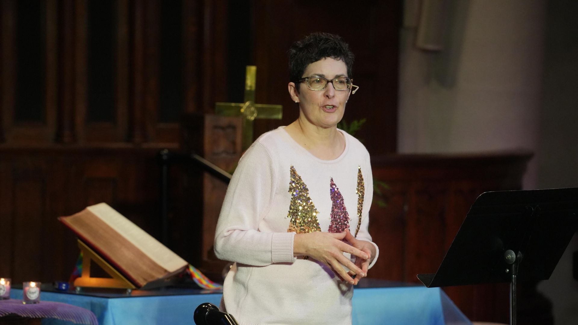 Pastor Mimi standing at a church podium beside an open Bible and music stand