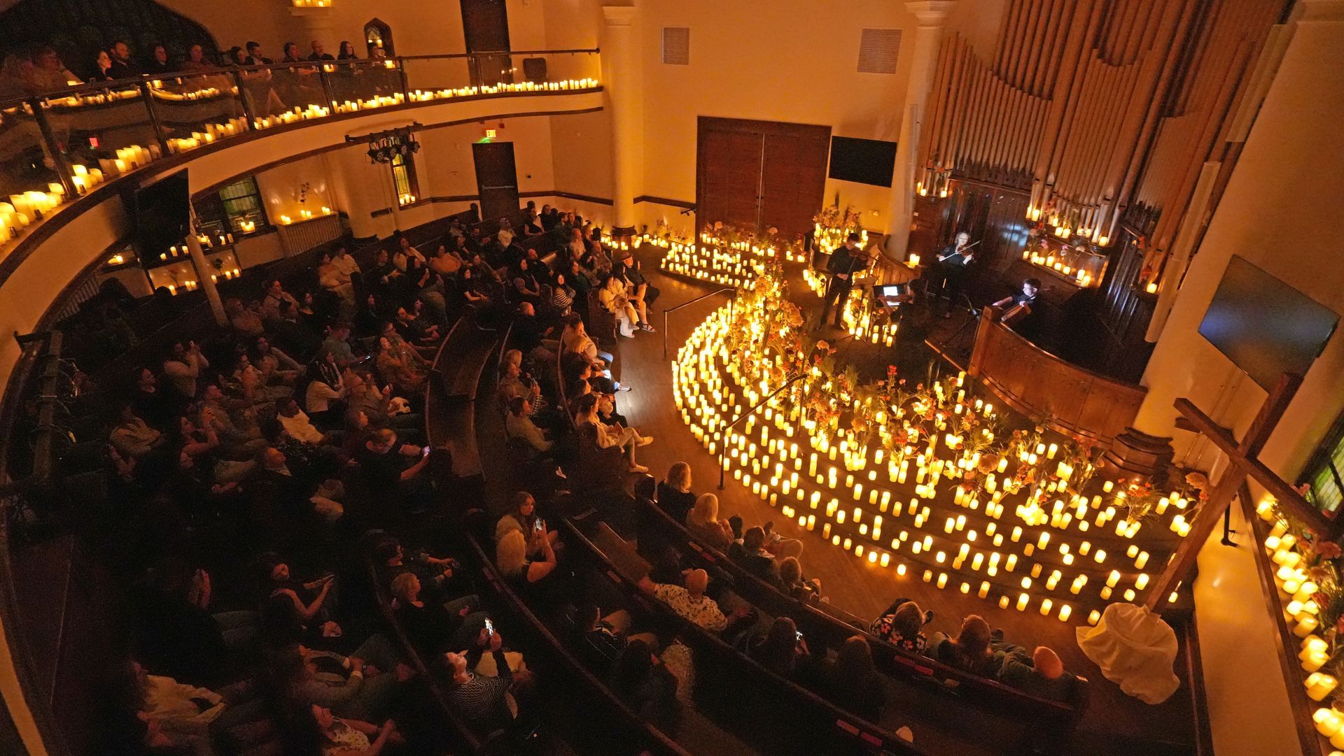 Short North Church. Candlelit concert in a grand hall, with a seated audience surrounding a glowing stage.