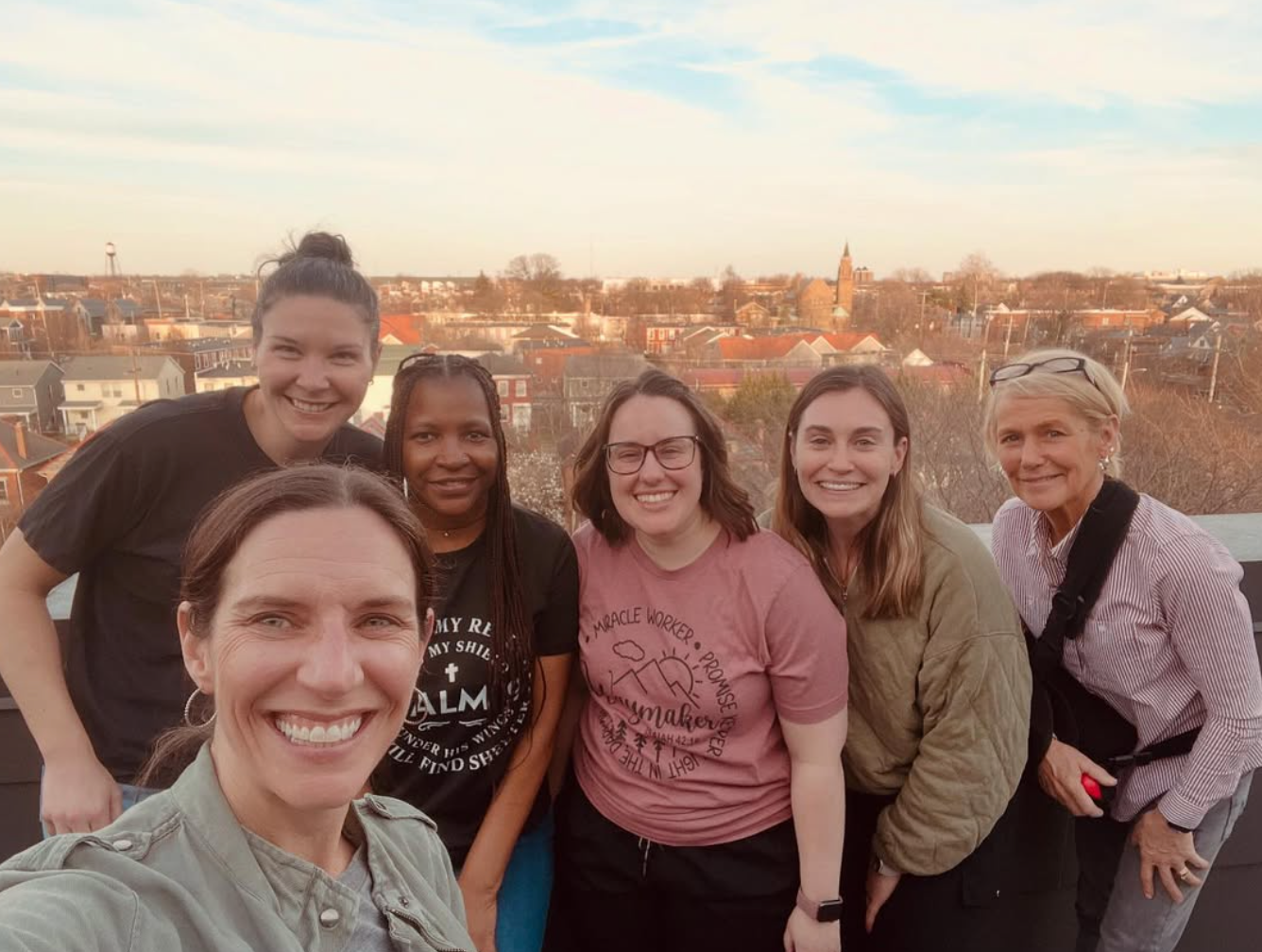Short North Church Soul Sisters. Six smiling friends posing on a rooftop at sunset with a city skyline behind them